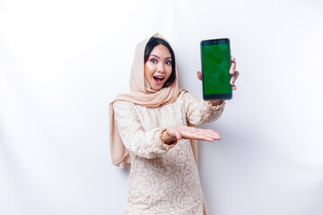 A portrait of a happy Asian Muslim woman wearing a hijab, showing her phone screen, isolated by white background