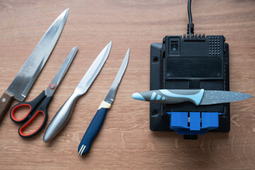 Sharpening a knife on an electric sharpener at home. Flatlay knife blade, scissors, sharpeners, dust flies on the machine.