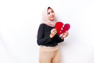 Beautiful young Asian Muslim woman expressed her sadness while holding broken heart isolated on white background
