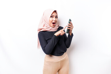 Shocked Asian woman wearing hijab, holding her phone, isolated by white background