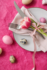 Table serving with Easter eggs and tulip flower on pink background