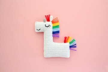 Crochet amigurumi handmade stuffed soft white unicorn toy with rainbow mane on pink background....