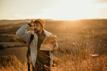 Shot of a young lost hiker holding a map while exploring golden hill fields. Travel and adventure concept
