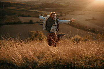 Happy man jumping in the air during a trekking tour in the hills on a sunset.