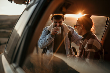 Fototapeta na wymiar Young couple talking, drinking a coffee watching the sunset from their car. Couple road travel together