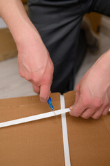 A man, a furniture assembler, opens a cardboard box with a clerical knife. The concept of unpacking the box.Close-up