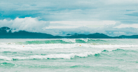 Coastline at sunrise or sunset, sea with waves against the backdrop of mountains, city and clouds