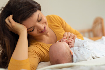 Mom talks and laughs with her newborn son at home bedroom
