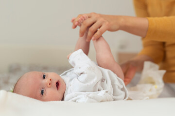 Mother changing her baby's diaper on bed - obrazy, fototapety, plakaty