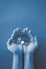 Two hand holding money coin on blue background with blue color filter. 