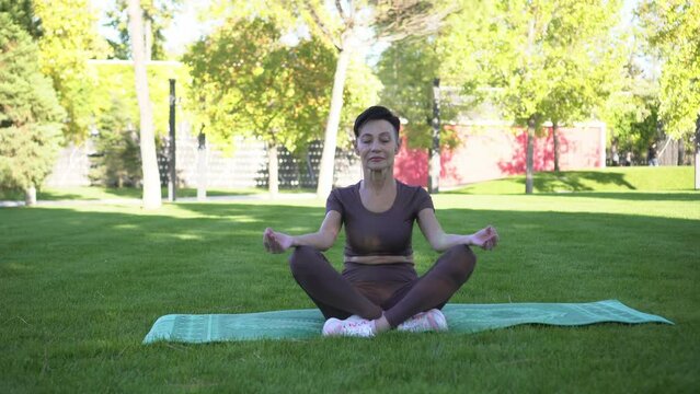 Active mature woman doing yoga or meditating in lotus position outdoors