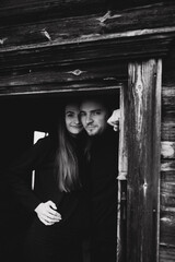 a man and a woman in black clothes near an old wooden house. photo in dark brown tones. old abandoned house and cloudy cold weather. beautiful stylish couple on the background of a brown wooden wall.