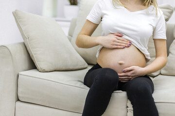 Crop photo of pregnant woman sitting on white sofa.