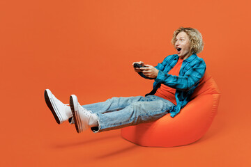Full body gambling young blond man wear blue shirt orange t-shirt sit in bag chair sit in bag chair...