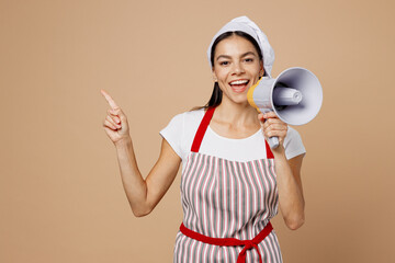 Young housewife housekeeper chef baker latin woman wear striped apron toque hat hold megaphone sream announces discounts sale Hurry up point aside isolated on plain beige background Cook food concept