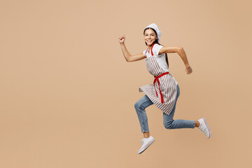 Fototapeta na wymiar Full body side view smiling happy fun young housewife housekeeper chef baker latin woman wear apron toque hat run fast look camera isolated on plain pastel light beige background. Cook food concept.