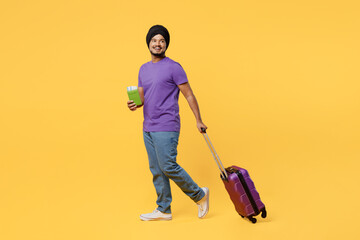 Traveler Sikh Indian man ties his turban dastar wearing t-shirt hold bag passport ticket isolated on plain yellow background. Tourist travel in free time rest getaway. Air flight trip journey concept.