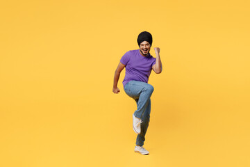Fototapeta na wymiar Full body fun devotee Sikh Indian man ties his traditional turban dastar wear purple t-shirt doing winner gesture celebrate clenching fists say yes isolated on plain yellow background studio portrait.