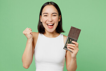 Young excited woman wears white clothes hold in hand dark chocolate bar do winner gesture isolated...