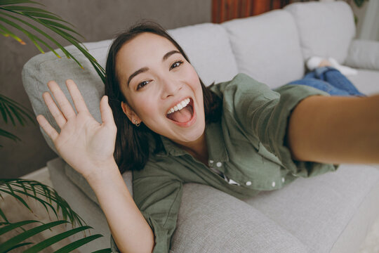 Full body close up young woman wear casual clothes doing selfie shot pov on mobile cell phone waving hand lay down on grey sofa stay at home hotel flat rest relax spend free spare time in living room