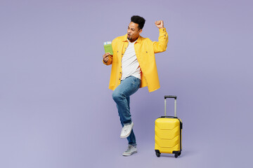 Full body traveler man wear casual clothes hold suitcase passport ticket do winner gesture isolated on plain purple background Tourist travel abroad in free time rest getaway. Air flight trip concept