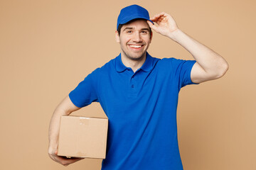 Fototapeta na wymiar Professional happy confident delivery guy employee man wear blue t-shirt uniform workwear touch cap work as dealer courier hold cardboard box isolated on plain light beige background. Service concept.