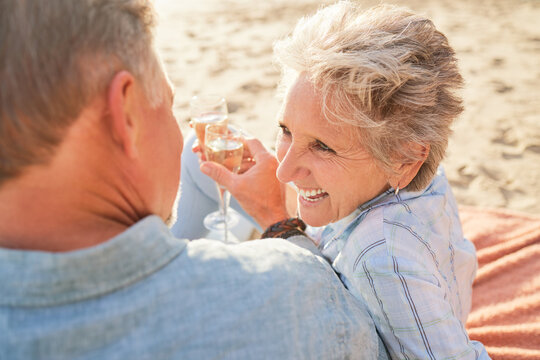 Champagne, Senior Beach Couple Laughing And Love With Mature Care And Support Of Marriage. Toast, Wine And Sea Picnic Of A Old Man And Woman Together On Holiday In Summer Loving The Sunshine Outdoor