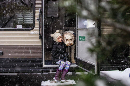 little girl sitting outside on steps of camper with big dog in snow