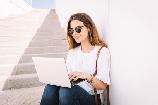 Front view of a happy student girl working with a laptop in the stairs of an university