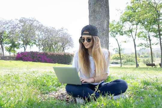 Front view of a happy student girl working with a laptop and smartphone in a green park of an university campus