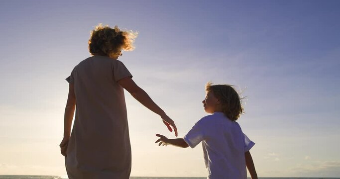 Blue sky with a soft summer sun against which mother and child walk hand in hand, illuminated by warm light rays. The concept of a bright future filled with joy and happiness that awaits them.
