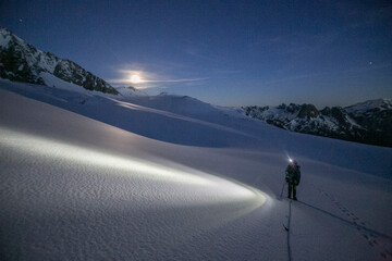 An alpinist uses a headlamp to navigate glaciated terrain pre dawn