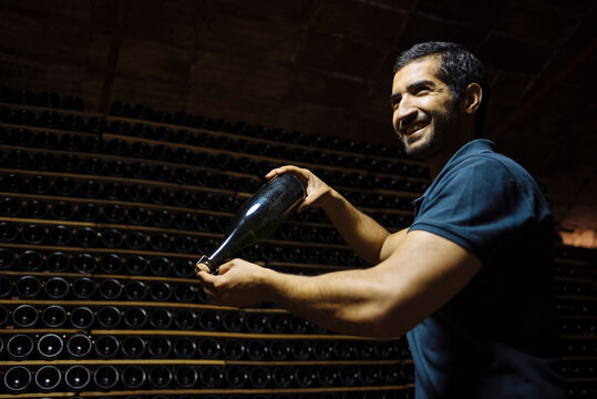 Cheerful man with sparkling wine bottle in cellar