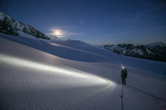 An alpinist uses a headlamp to navigate glaciated terrain pre dawn