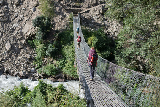 Hikers walking on skinny bridge over canyon and river in Asia