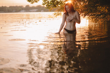 Topless woman covering her breast while standing in lake at sunset