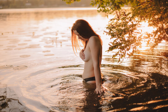 Sensual topless woman covering her breast while standing in lake