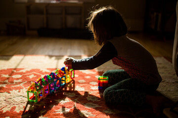 A child sits on the floor in golden morning light building with tiles
