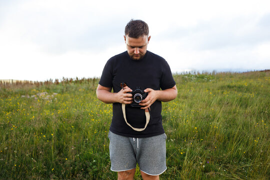 guy in a black t-shirt with a camera in his hands among the mountains