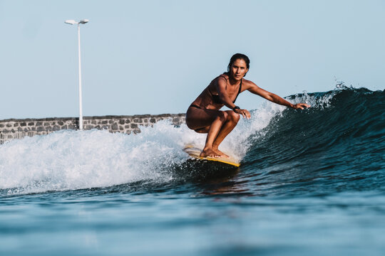 Full length action of female surfer on yellow surfboard