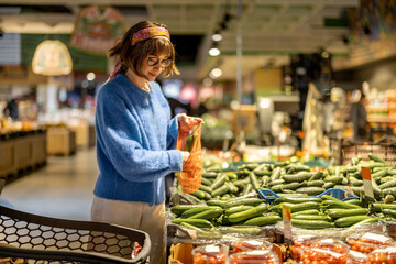 Young woman chooses vegetables and puts them into mesh bag at supermarket. Concept of buying vegetables and use of reusable bags for groceries in supermarkets