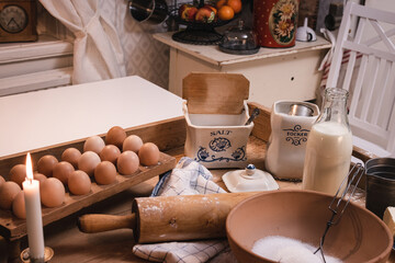 Ingredients for Christmas baking in a country kitchen, milk, salt, eggs, candle light, flour, sugar, rolling pin, standing on an old baking table.