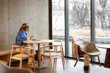 Young adult woman works on a digital tablet while sitting at modern coffee shop. Concept of remote creative work online