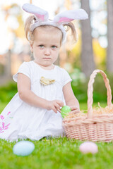 Little girl wearing bunny ears on Easter day hunts for Easter eggs on the lawn