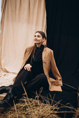 Obraz premium beautiful girl in a black sweater and black pants and a beige coat on a black and beige fabric background. cold cloudy weather and dry yellow tall grass and a girl. stylish fashion portrait. 