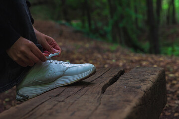 A runner or jogger woman tying her white sneaker in the forest