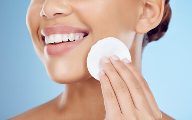 Skincare, smile and woman with cotton pad on face, removing makeup or dirt removal with luxury skin product in studio. Dermatology, cosmetics and facial for happy model isolated on blue background. © Emily Norris/peopleimages.com