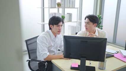 Two young asian businessmen discussing financial market data and using computer on desk at office