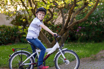 Fototapeta premium Happy school kid boy having fun with riding of bicycle. Active child with safety helmet making sports with bike in nature. Safety, sports, leisure with kids concept