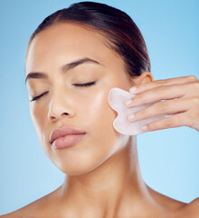 Woman, beauty and face massage with gua sha, facial product or aesthetic skincare in studio. Young...